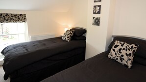 A bedroom with two beds, a radiator, and three wall-mounted pictures. - Somer Leyton Cottage (Hogsthorpe, near Chapel St Leonards)