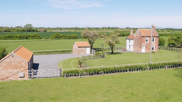A rural landscape with a brick house, a smaller brick structure, and a fenced field. - Somer Leyton Cottage (Hogsthorpe, near Chapel St Leonards)