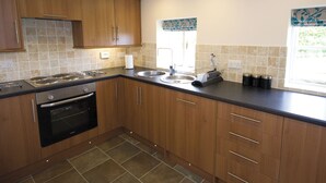 A modern kitchen with wooden cabinets, a built-in oven, a sink, and a window with a view. - Somer Leyton Cottage (Hogsthorpe, near Chapel St Leonards)