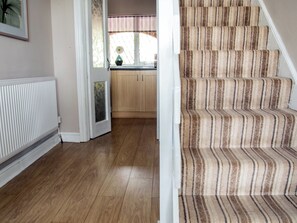 A staircase with striped carpet, a wooden floor, a radiator, and a door leading to a kitchen area. - 3 bedroom accommodation in Addlethorpe (Addlethorpe)
