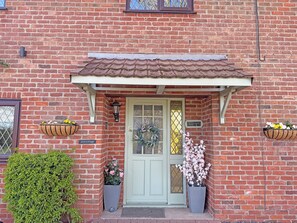 A brick building with a green door, two flower baskets, a small potted plant, and a sign reading 'Ash Cottage.' - 3 bedroom accommodation in Addlethorpe (Addlethorpe)