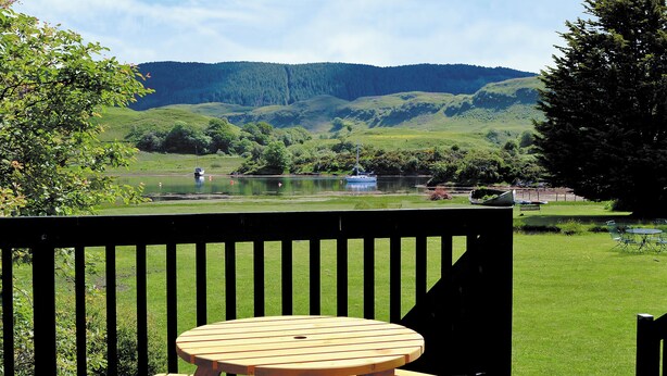 A wooden deck with a picnic table and chairs overlooking a lake with boats and hills in the background. - 2 bedroom accommodation in Clachan Seil, near Oban (Clachan Seil, near Oban)