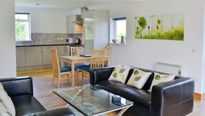 A modern living room with a glass coffee table, leather sofa, and a dining area with wooden chairs and a small table. - 2 bedroom accommodation in Clachan Seil, near Oban (Clachan Seil, near Oban)