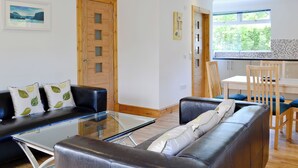 A modern living room with a glass coffee table, a black leather sofa, and a wooden dining table with chairs. - 2 bedroom accommodation in Clachan Seil, near Oban (Clachan Seil, near Oban)