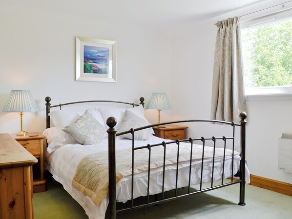 A neatly made bed with white linens and a wooden headboard. There are two bedside tables, each with a lamp and a small wooden nightstand. A framed picture hangs on the wall above the bed. - 2 bedroom accommodation in Clachan Seil, near Oban (Clachan Seil, near Oban)