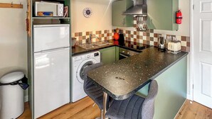 A compact kitchen with a washing machine, a toaster, and a fire extinguisher. - 1 bedroom accommodation in North Newton (North Newton)