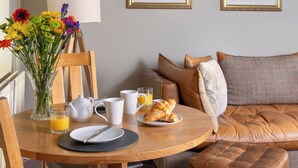 A breakfast setup with a table, chairs, a vase of flowers, a coffee pot, cups, a glass of orange juice, and croissants. - 1 bedroom accommodation in Keswick (Keswick)