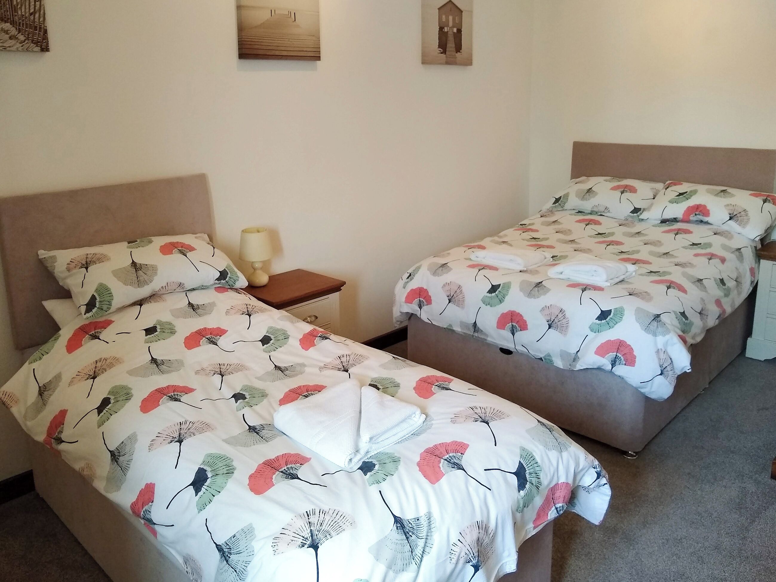 Een kamer met twee bedden, elk voorzien van een bloemenprintdeken, een nachtkastje met een lamp en een aan de muur hangend schilderij.