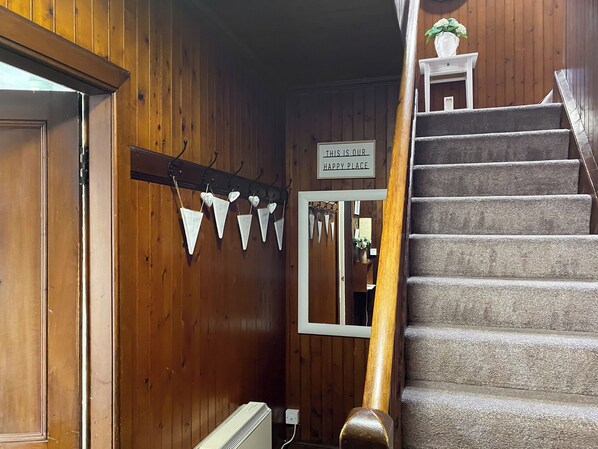 Un intérieur en bois avec un escalier, une pancarte sur laquelle on peut lire « ICI, C’EST NOTRE PETIT COIN DE BONHEUR », et des décorations triangulaires.