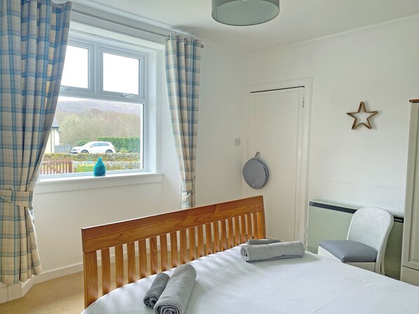 A bedroom with a wooden bed, a window with curtains, a radiator, a chair, and a star decoration on the wall.