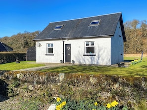 Une maison à deux étages, avec un toit noir, des murs blancs et une porte d’entrée ornée d’un motif en forme de cœur.