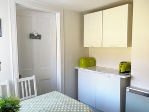 A compact kitchen with white cabinets, a green appliance, and a white door with a sign.