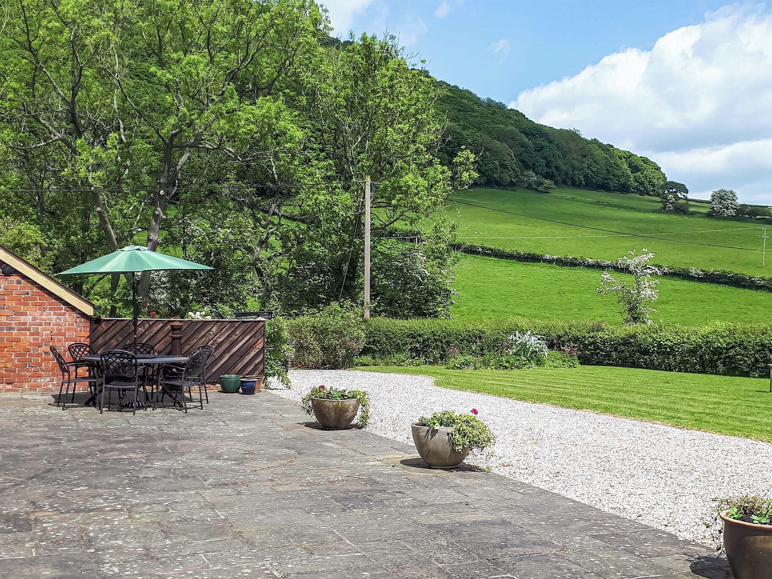 A patio with outdoor furniture and a brick wall, surrounded by lush greenery and a view of rolling hills.