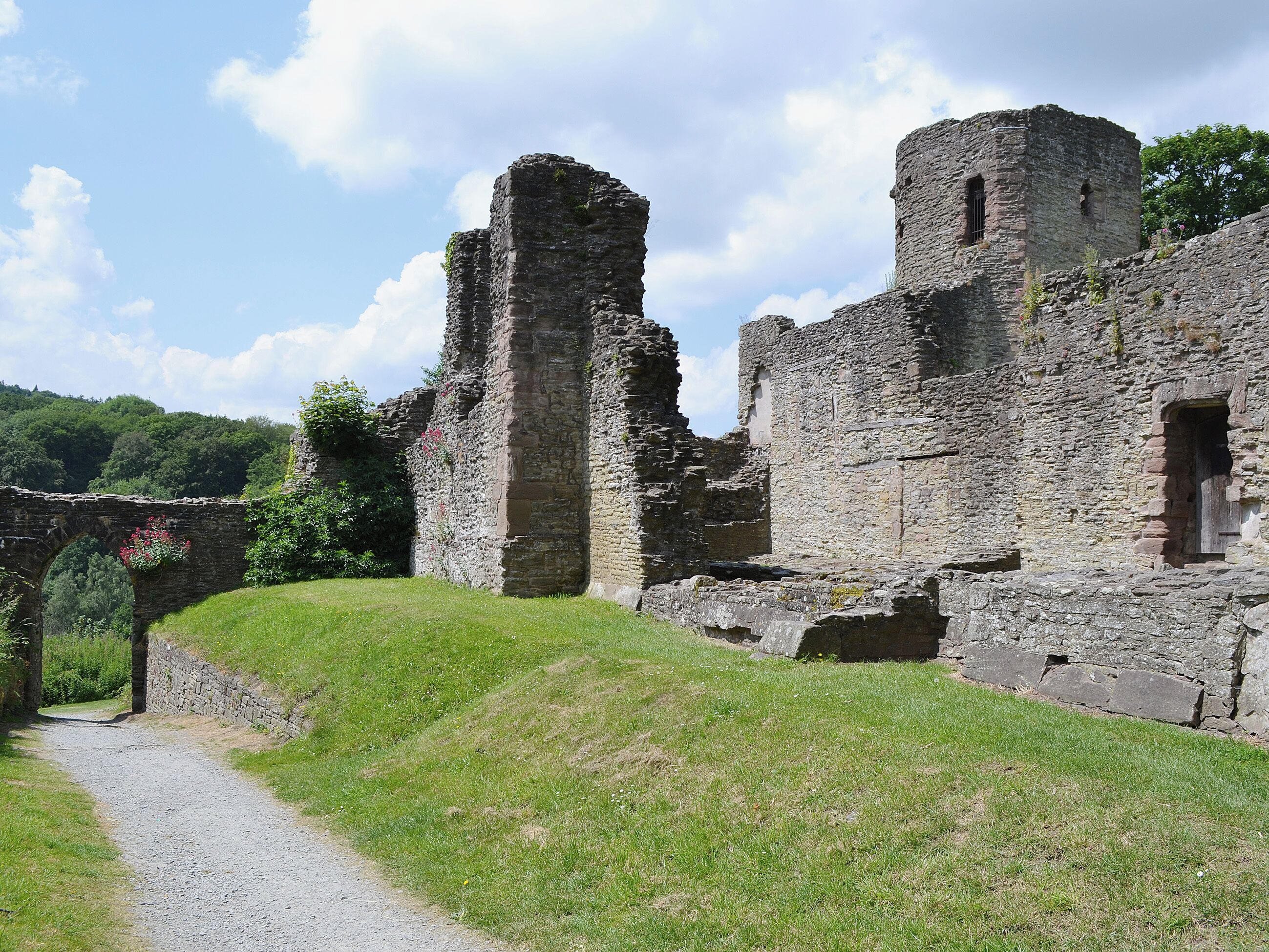 Ruínas de uma estrutura de pedra medieval, com um caminho gramado serpenteando por elas.