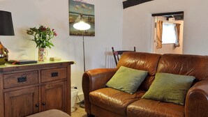 Ein gemütliches Wohnzimmer mit einem braunen Ledersofa, einer Holzkommode und einem Bild an der Wand.