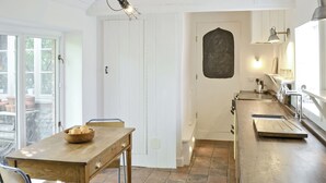 Una cocina con una mesa de madera, sillas, un cuenco de fruta y piso de baldosas.