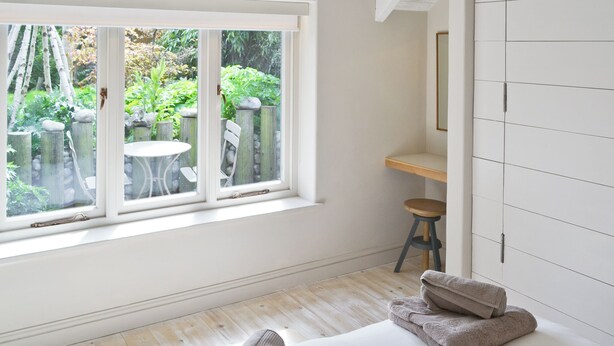 Una habitación con un ventanal grande, una mesita y una silla afuera.
