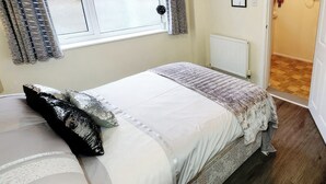 A bedroom with a bed, a window with curtains, a radiator, and a door leading to another room. - 1 bedroom accommodation in Horning, near Norwich (Horning, near Norwich)