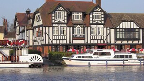 A traditional Tudor-style building with a sign for 'The Swan Inn' and a boat docked in front. - 1 bedroom accommodation in Horning, near Norwich (Horning, near Norwich)