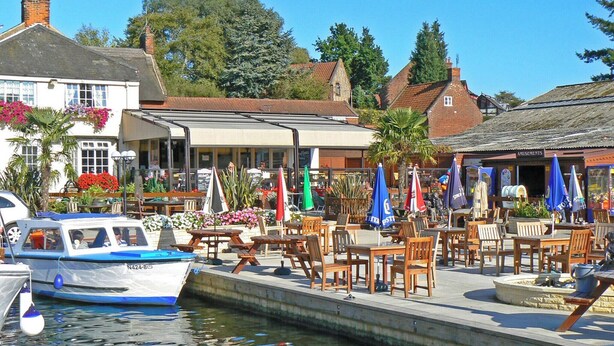 A riverside café with outdoor seating, a boat docked nearby, and traditional buildings in the background. - 1 bedroom accommodation in Horning, near Norwich (Horning, near Norwich)