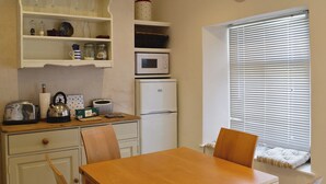 A compact kitchen with white cabinetry, a microwave, a refrigerator, and a dining table with chairs. - 2 bedroom accommodation in Calstock (Calstock)