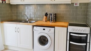 A kitchen with white cabinets, a stainless steel sink, a built-in washing machine, and a built-in oven. - 2 bedroom accommodation in Calstock (Calstock)