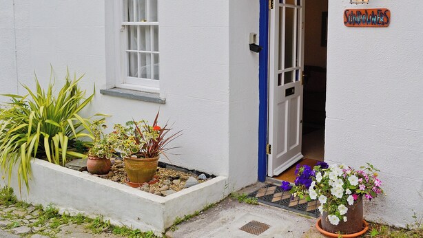 A white building with a blue door, a window, and a sign that reads "Sundowners". There are potted plants outside. - 2 bedroom accommodation in Calstock (Calstock)