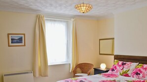 A bedroom with a bed, a chair, a bedside table, a window with curtains, a picture on the wall, and a ceiling light. - 2 bedroom accommodation in Calstock (Calstock)