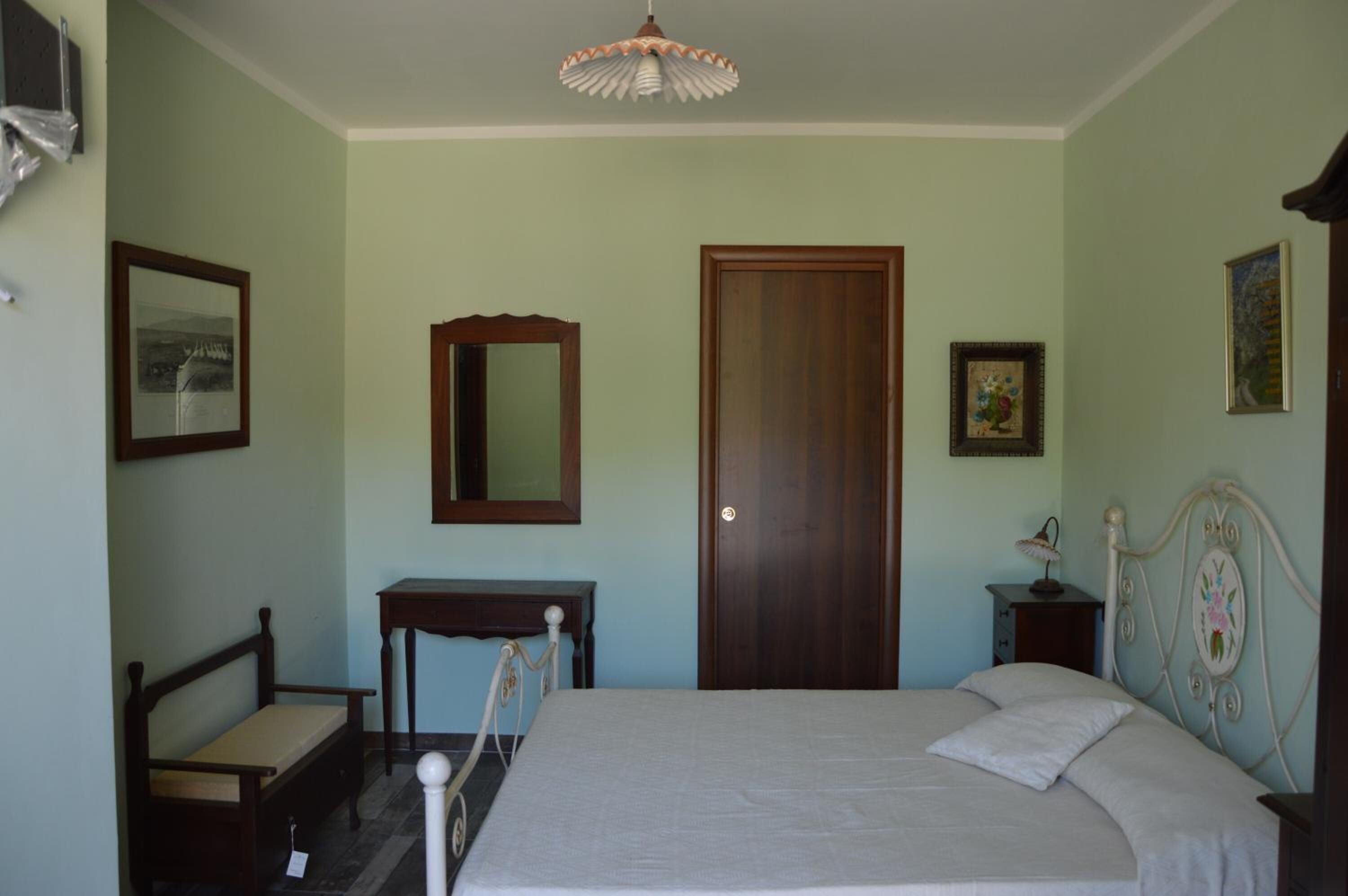 A bedroom with a bed, a wooden bench, a small table, a mirror, and a door.