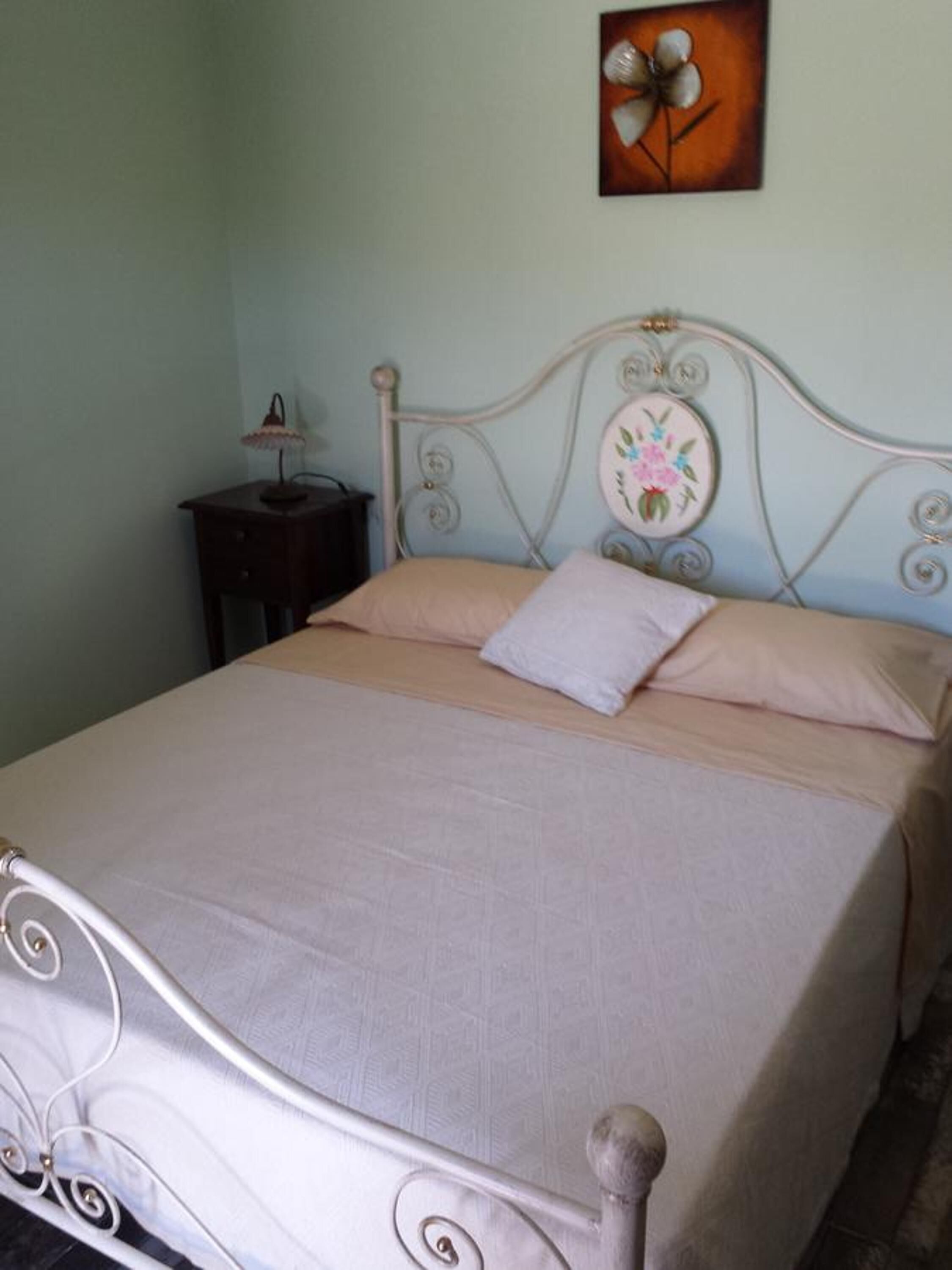 Una cama bien hecha con estructura metálica y cabecera floral.