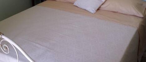 Una cama bien hecha con estructura metálica y cabecera floral.