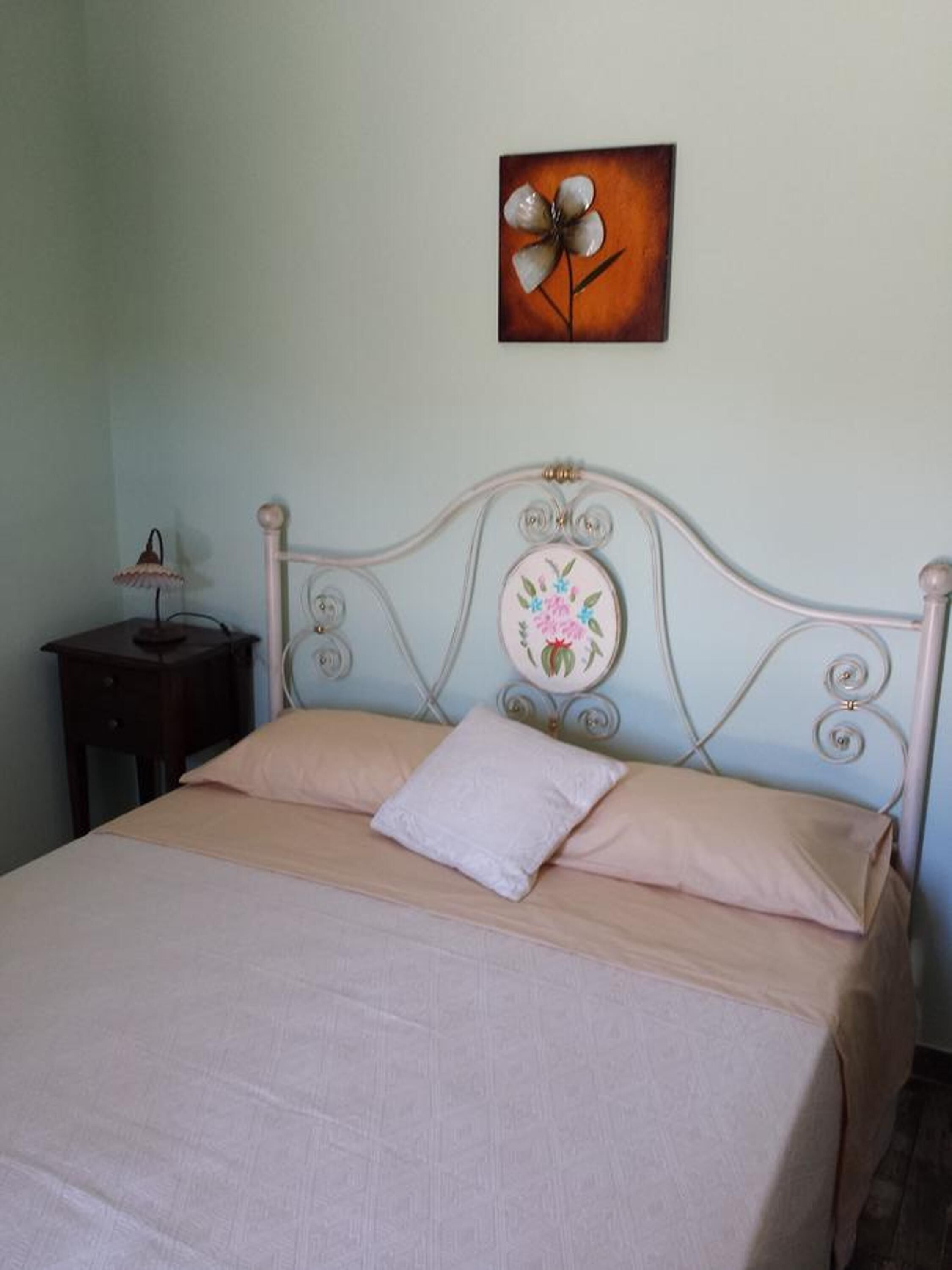 A bed with a headboard, a bedside table with a lamp, and a wall-mounted painting.