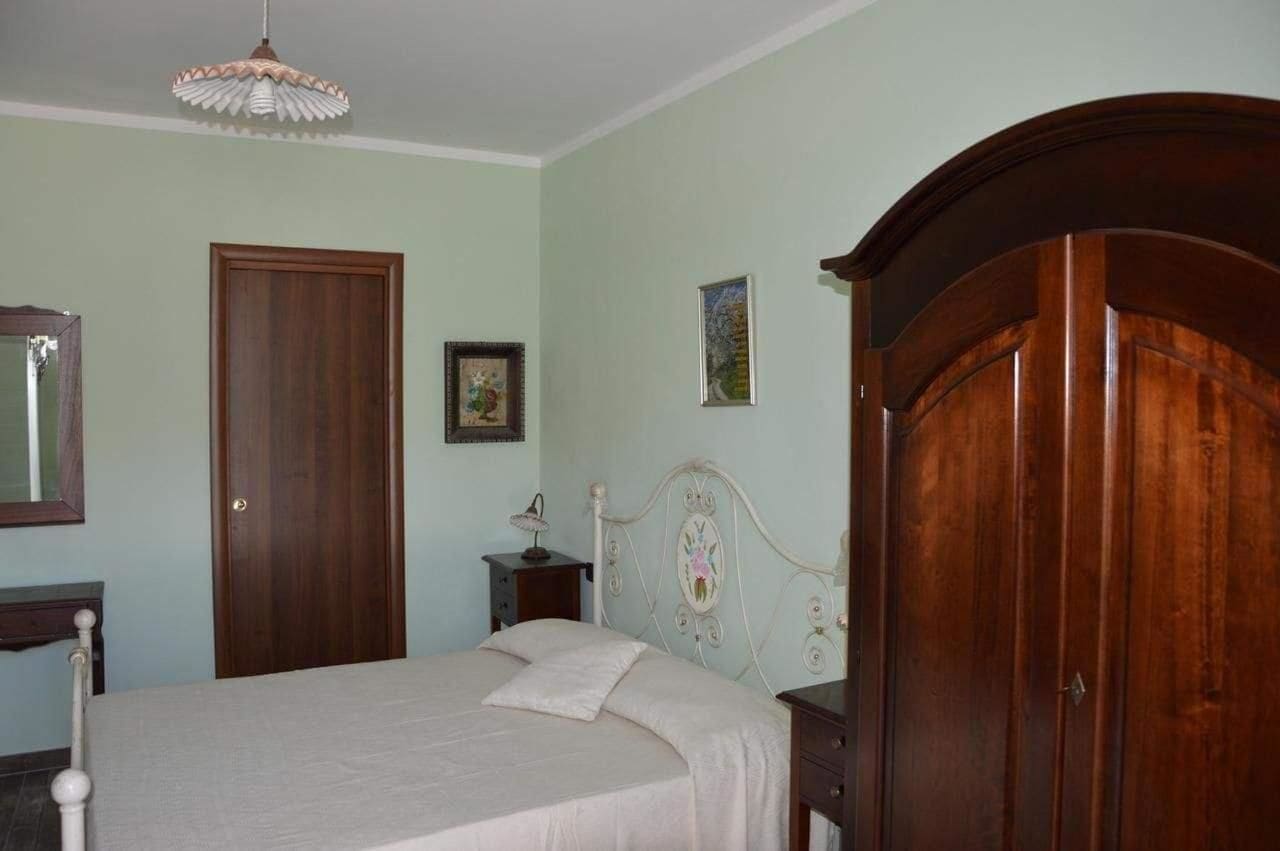 Een slaapkamer met een bed, een houten garderobe, een nachtkastje en een hanglamp.