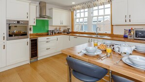 Une cuisine moderne avec des meubles blancs, des appareils en acier inoxydable et une table à manger en bois, mise pour le petit-déjeuner.