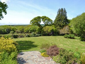 Un jardin bien entretenu, avec un chemin de pierre, une végétation luxuriante et un grand arbre.