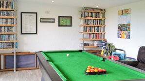 Ein Billardtisch mit grüner Spielvliesfläche, umgeben von Bücherregalen voller Bücher.