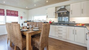 A modern kitchen with white cabinets, a wooden dining table, and woven chairs. - Swedish timber-style house, with sauna and hot tub, on a 400-acre estate. (Fritton, near Great Yarmouth)