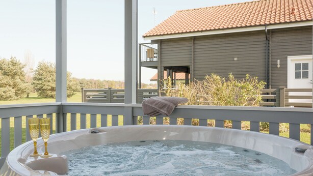 A hot tub on a covered deck with a view of a house and trees. - Swedish timber-style house, with sauna and hot tub, on a 400-acre estate. (Fritton, near Great Yarmouth)