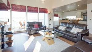 A spacious living room with a leather sofa, a glass coffee table, and a dining area with a table and chairs. - Swedish timber-style house, with sauna and hot tub, on a 400-acre estate. (Fritton, near Great Yarmouth)