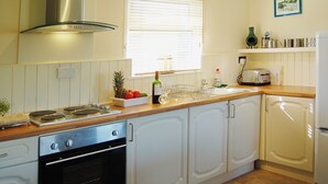 A kitchen with white cabinets, a stove, an oven, a sink, and a window with blinds. - Enjoy distant sea views whilst relaxing amidst the stunning rural surroundings. (St Merryn, near Padstow)