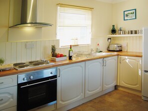 A kitchen with white cabinets, a stove, an oven, a sink, and a window with blinds. - Enjoy distant sea views whilst relaxing amidst the stunning rural surroundings. (St Merryn, near Padstow)
