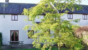Un edificio blanco con techo oscuro, un banco de madera y un árbol en primer plano.