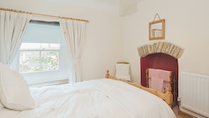 Une chambre à coucher avec un lit, une fenêtre avec des rideaux, une cheminée et un miroir au mur.