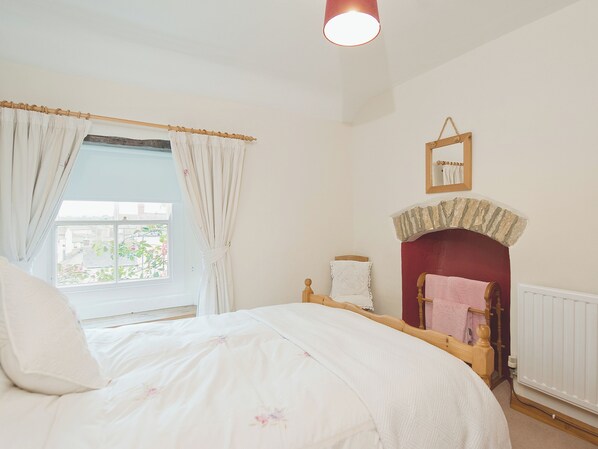 A bedroom with a bed, a window with curtains, a fireplace, and a mirror on the wall.