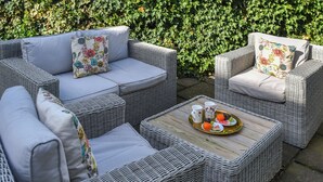 A wicker outdoor seating area with cushions and a tray of fruit and drinks. - Captain's Cottage - 27888 (Winterton-on-Sea)