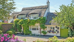 A traditional thatched-roof house with multiple windows, a chimney, and a green gate. - Captain's Cottage - 27888 (Winterton-on-Sea)