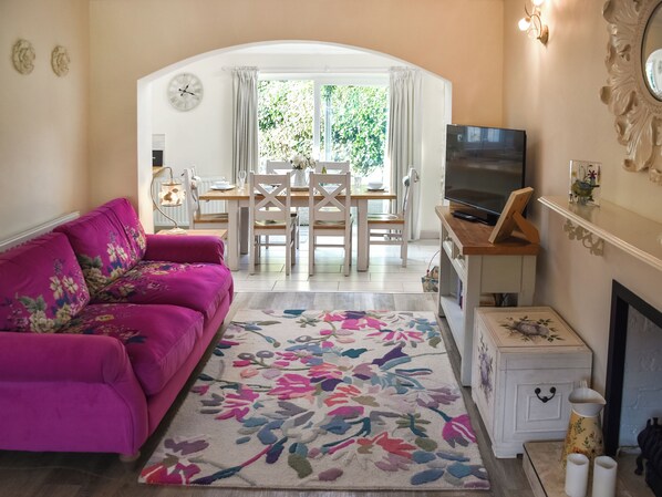 A living room with a pink sofa, a TV, a fireplace, and a dining area with a table and chairs.