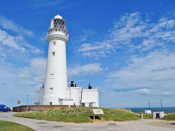 A white lighthouse with a weather vane, a signboard, and a small building with a blue door. - 2 bedroom accommodation in Flamborough (Flamborough)
