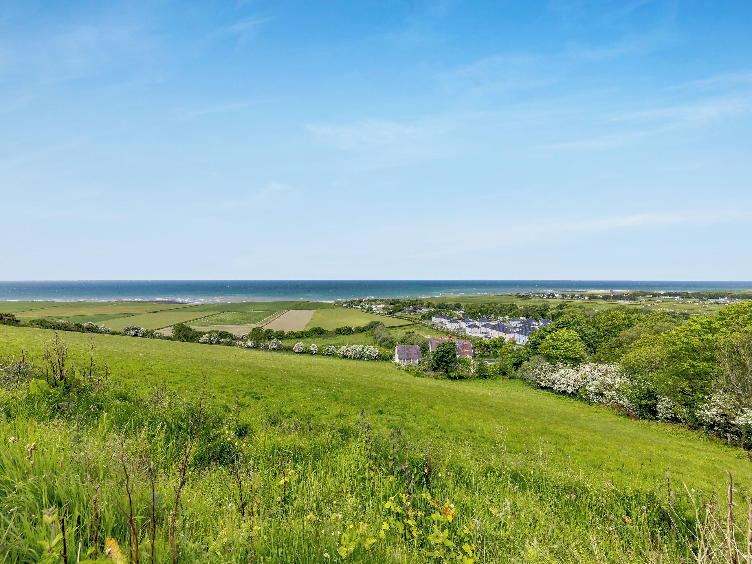 A coastal landscape with fields, a small cluster of houses, and a view of the sea.