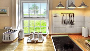 A kitchen with a window, a toaster, a tray with cookies, a stove, and hanging utensils. - 2 bedroom accommodation in Happisburgh, near Cromer (Happisburgh, near Cromer)